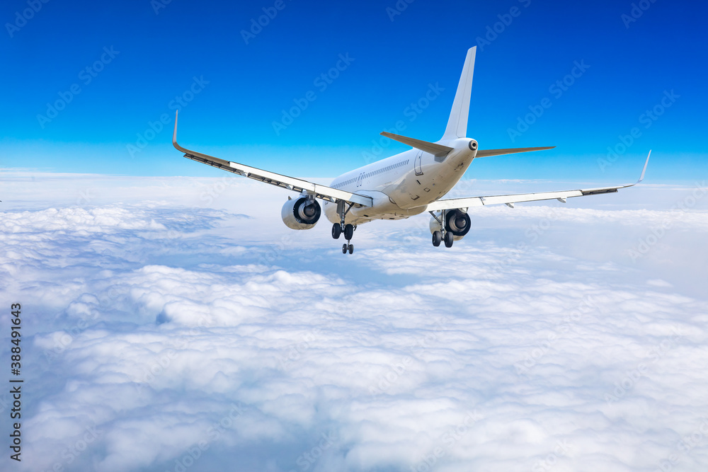 Commercial airplane flying above blue sky and white clouds.