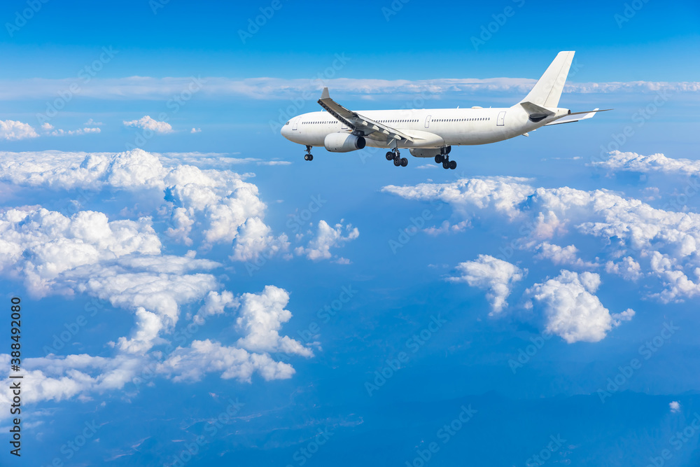 Commercial airplane flying above blue sky and white clouds.