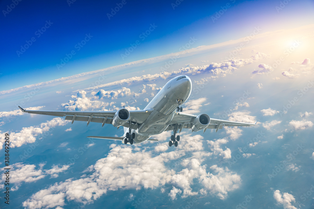 Commercial airplane flying above blue sky and white clouds.