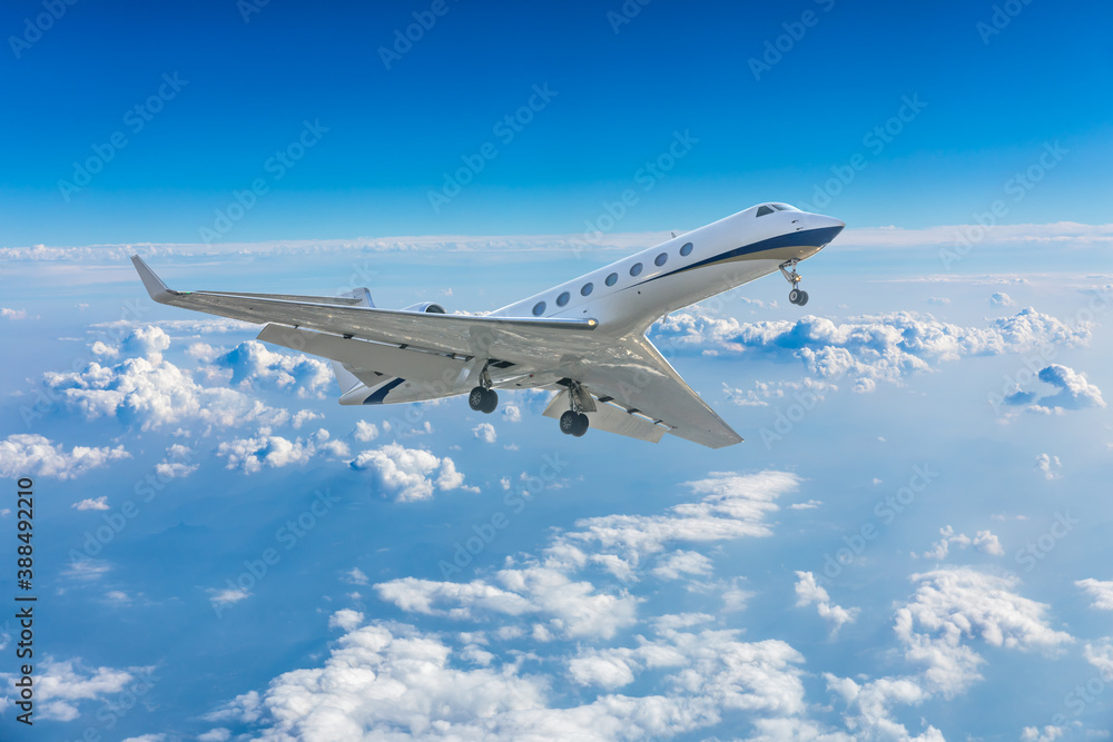 Commercial airplane flying above blue sky and white clouds.