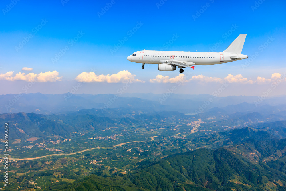 Commercial airplane flying above blue sky and white clouds.