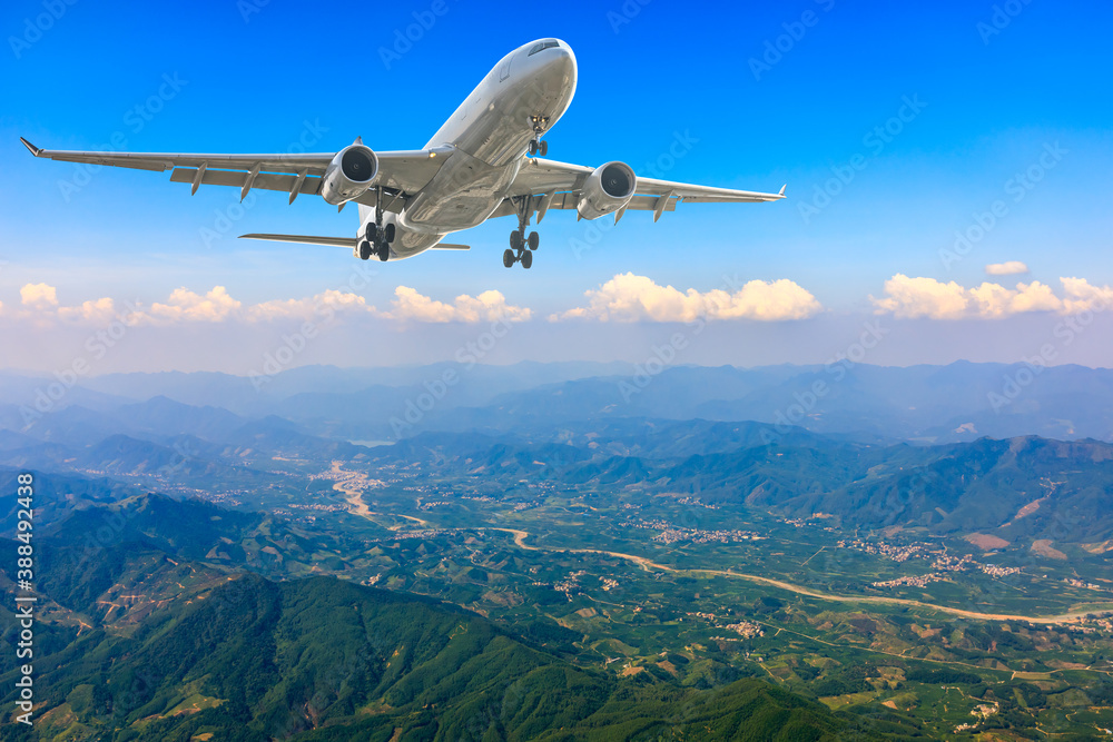 Commercial airplane flying above blue sky and white clouds.