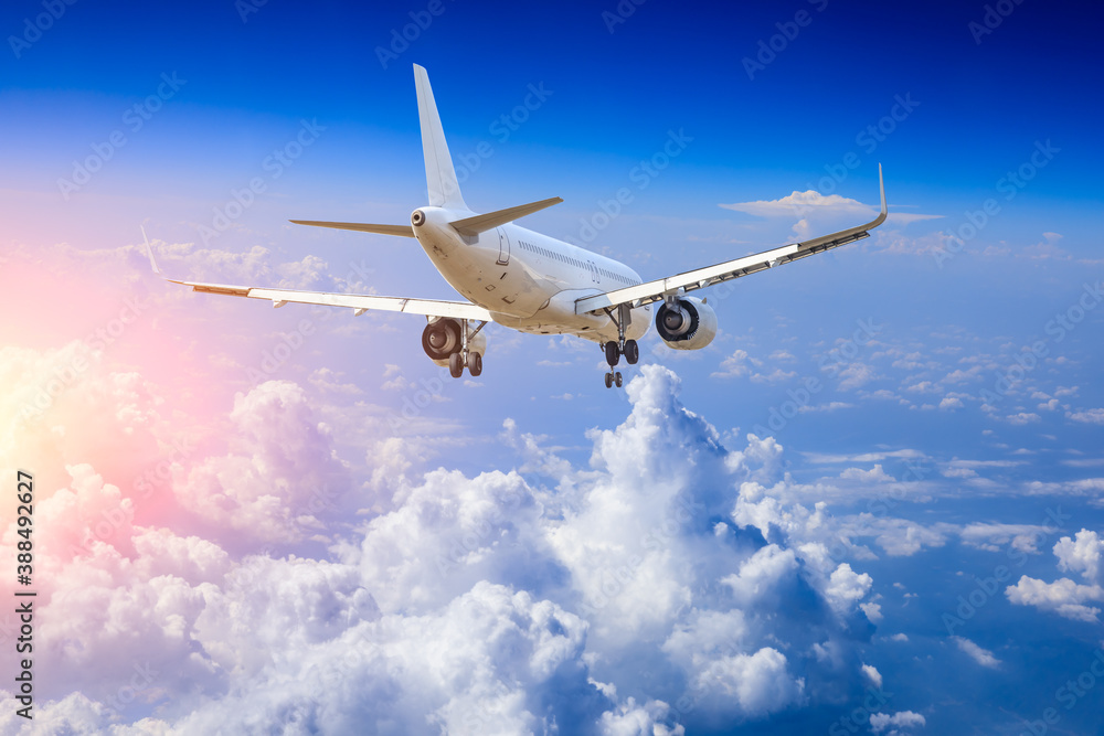 Commercial airplane flying above blue sky and white clouds.