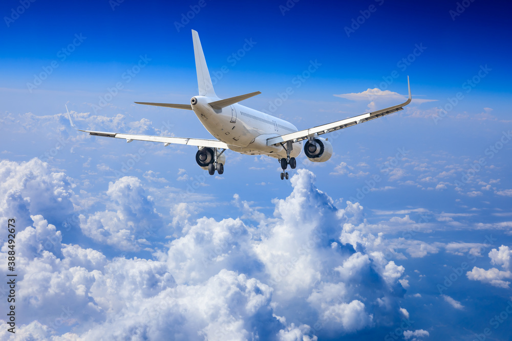 Commercial airplane flying above blue sky and white clouds.