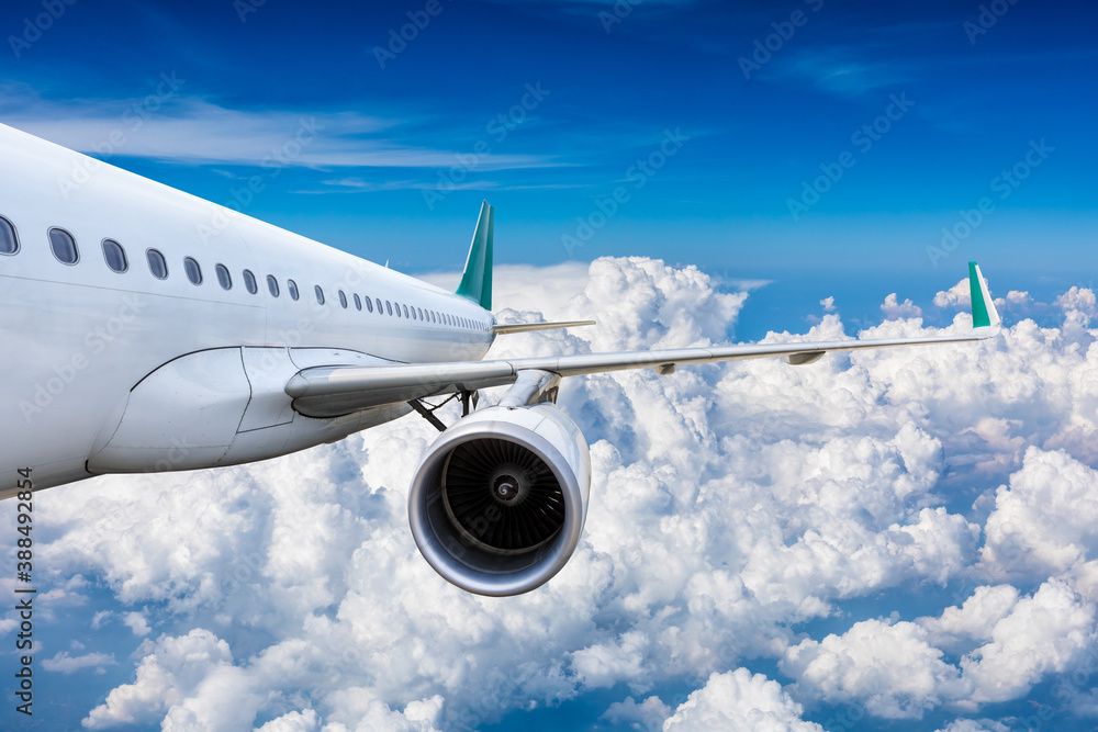 Commercial airplane flying above blue sky and white clouds.