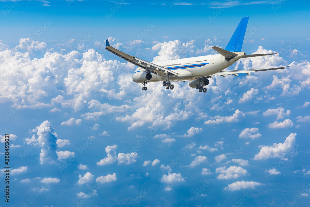 Commercial airplane flying above blue sky and white clouds.