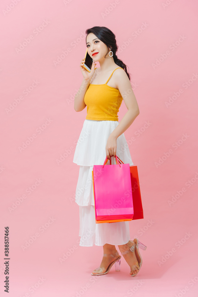 Portrait of a pretty happy girl talking on mobile phone while holding shopping bags over pink backgr