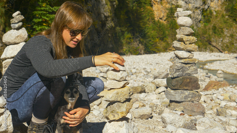 CLOSE UP: Hiker kneels next to her dog to stack rocks into a beautiful tower.