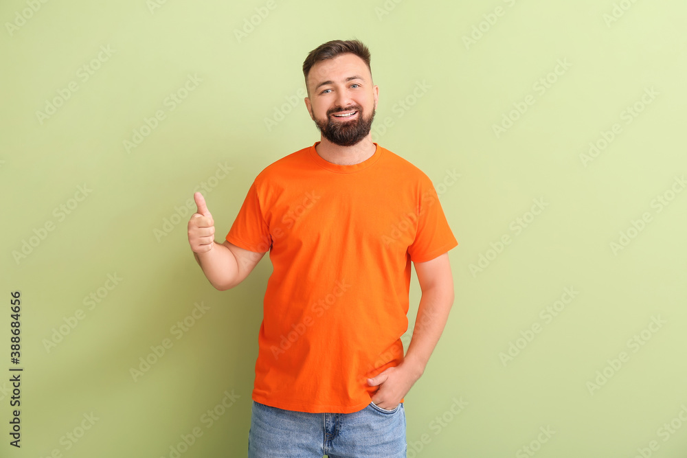 Handsome man in orange t-shirt showing thumb-up on color background