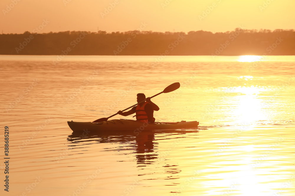 Young man kayaking in river at sunset