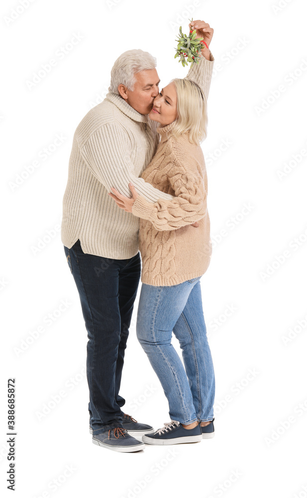 Mature man kissing his wife under mistletoe branch on white background