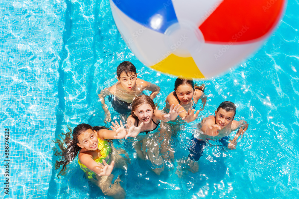 Many kids in swimming pool play with inflatable ball view from above reaching hands up