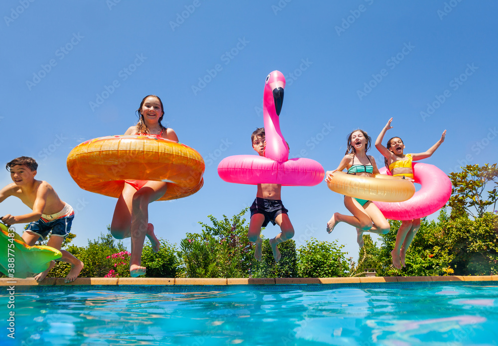 Group of happy little kids dive in water with inflatable toys flamingo doughnut jump into the swimmi