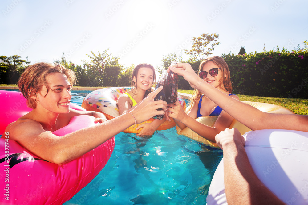 Group of children cheer and celebrate partying in the swimming pool drink soda from bottles