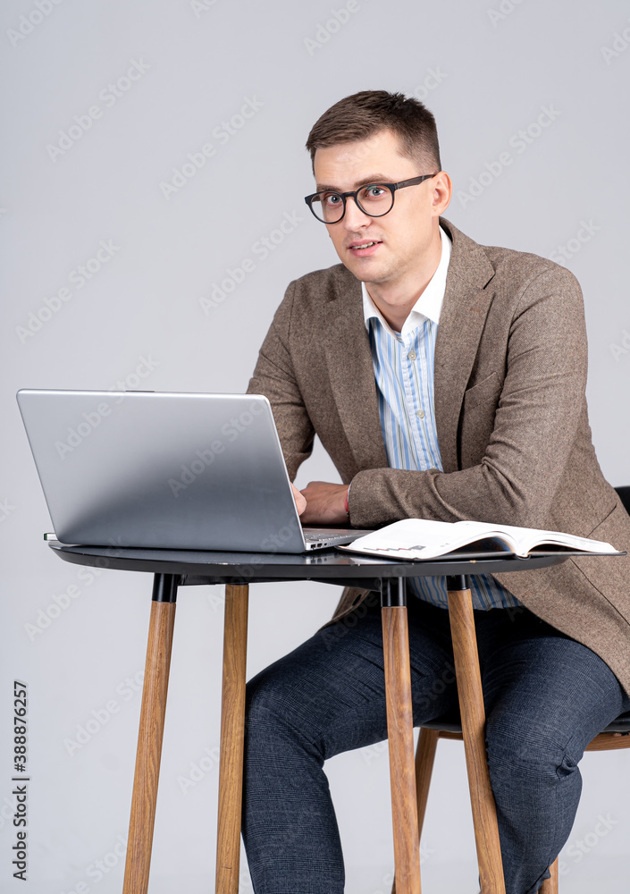 Businessman with a laptop on desk. Guy in suit isolated over gray background.