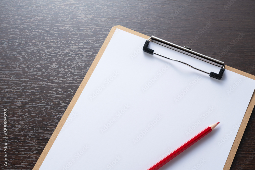 A clipboard with white paper and a red pencil on a wooden background