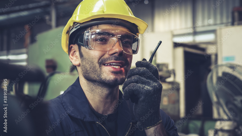 Factory worker talking on portable radio while inspecting machinery parts . Industrial and engineeri