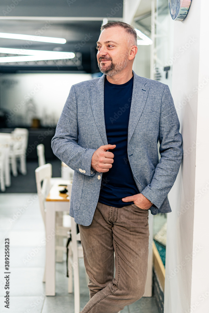 Happy senior businessman standing over grey wall and looking at side. Portrait of successful leader 