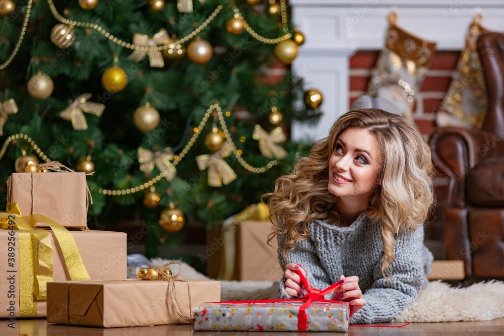 Nice blonde with christmas presents near new year tree. Luxury interior before holiday.