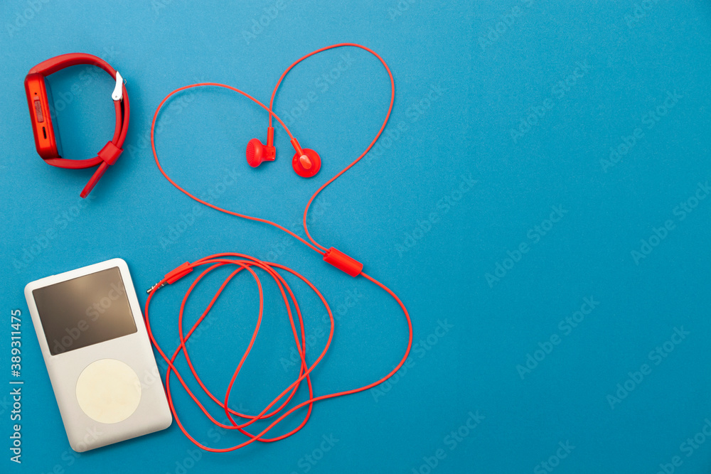 Close up of red earphones with sport watch and music player on blue paper background.