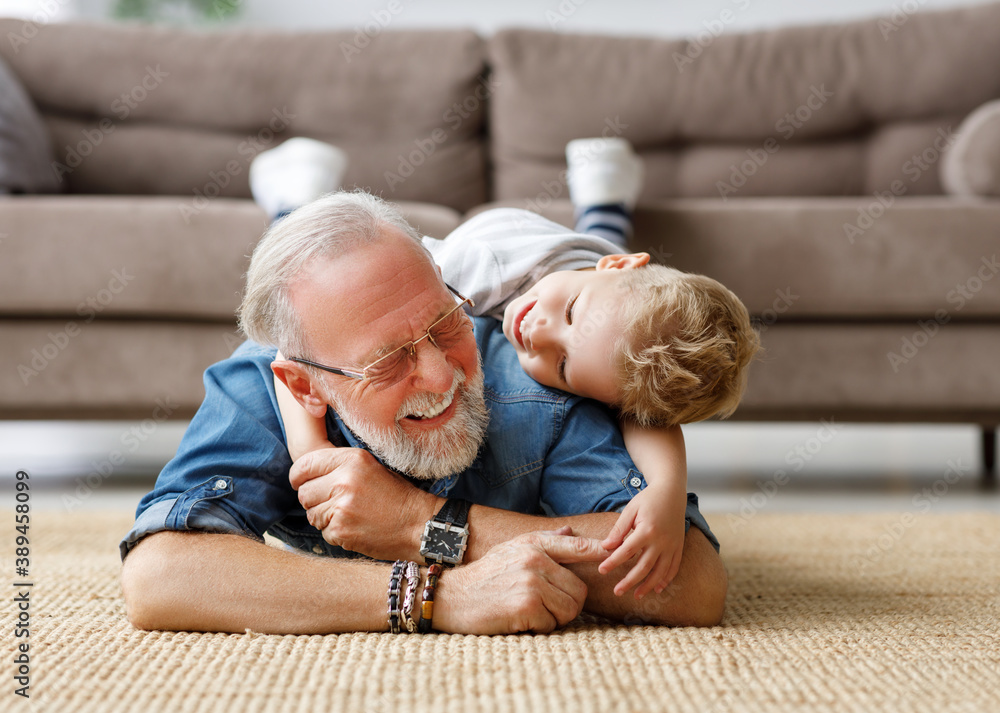 Cheerful kid boy hugging grandfather at home.