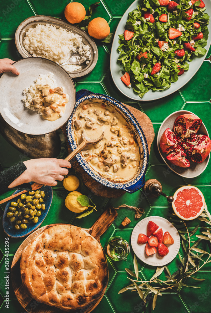 Turkish style family dinner. Flat-lay of female hands serving Turkish lamb in yogurt sauce over tabl