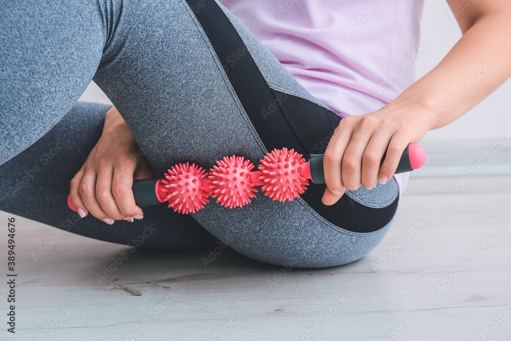 Sportswoman massaging herself with body roller indoors