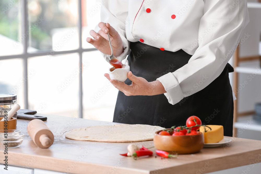 Mature female chef making tasty pizza in kitchen