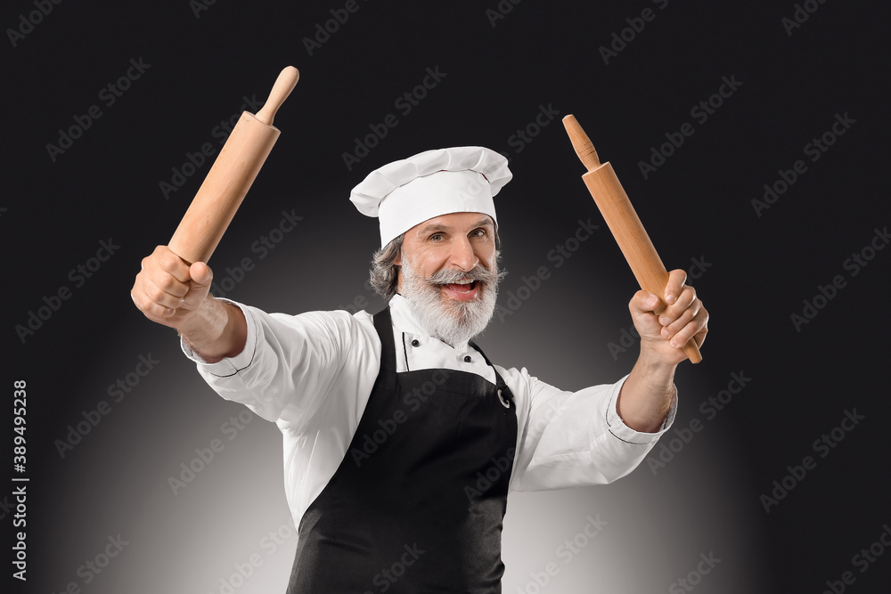 Mature male chef with rolling pins on dark background