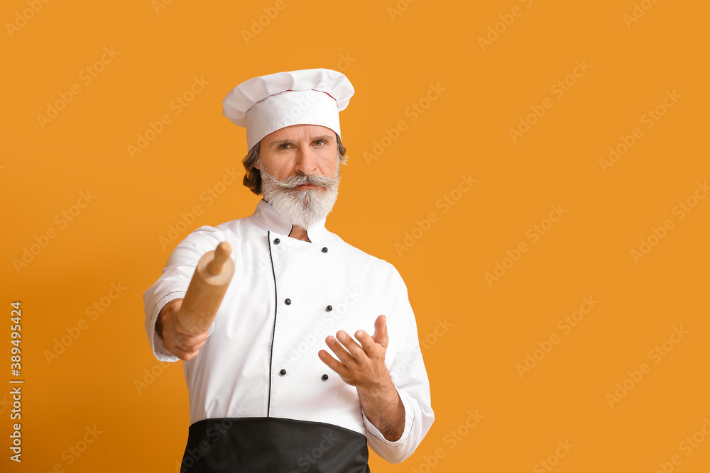 Mature male chef with rolling pin on color background