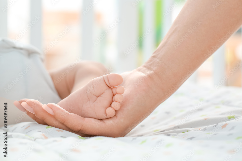 Mothers hand holding tiny leg of her baby lying in crib