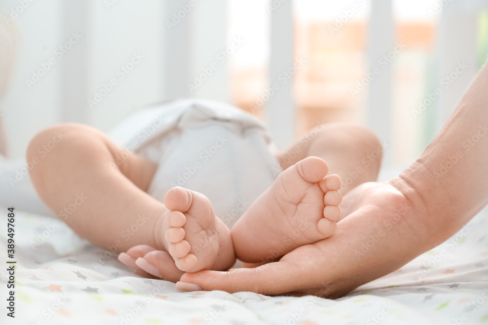 Mothers hand holding tiny legs of her baby lying in crib