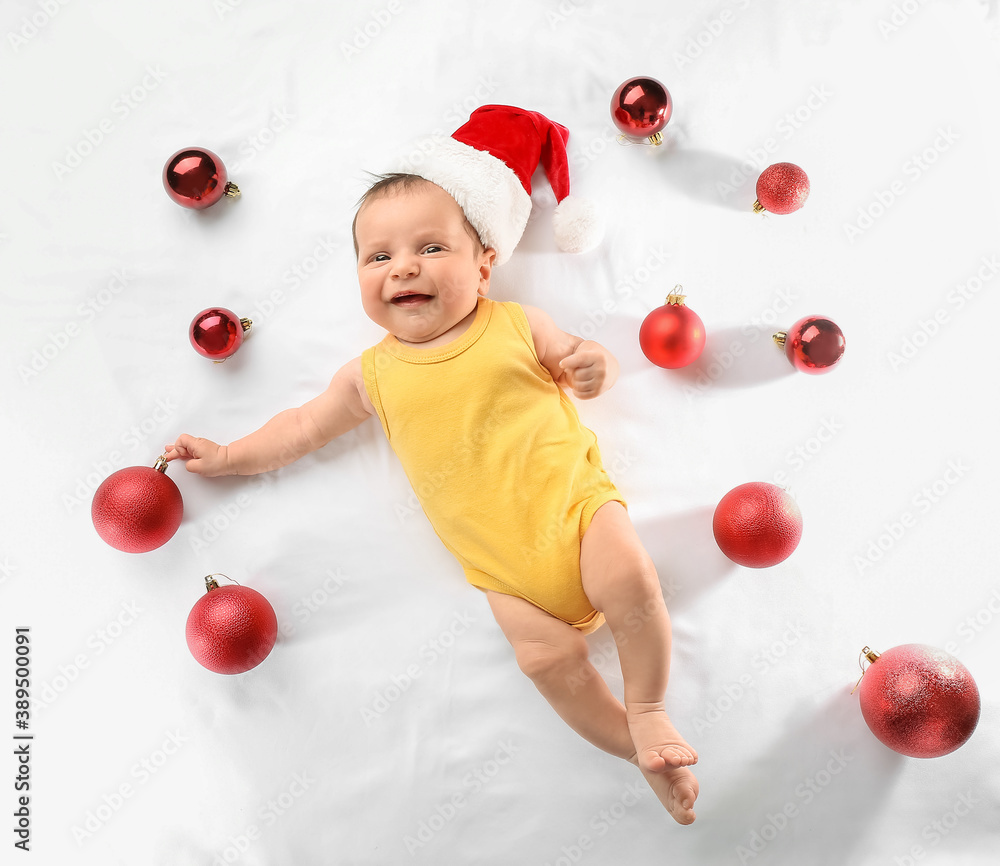 Cute little baby in Santa hat and with Christmas balls on white background