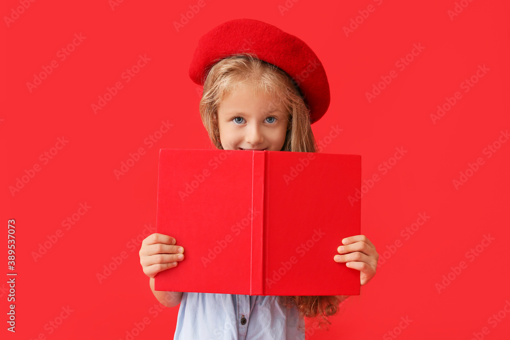 Cute little girl in autumn clothes and with book on color background