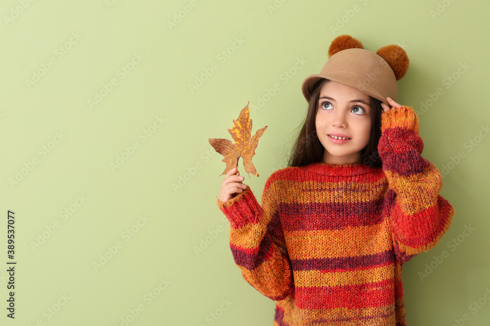 Cute little girl with autumn leaf on color background