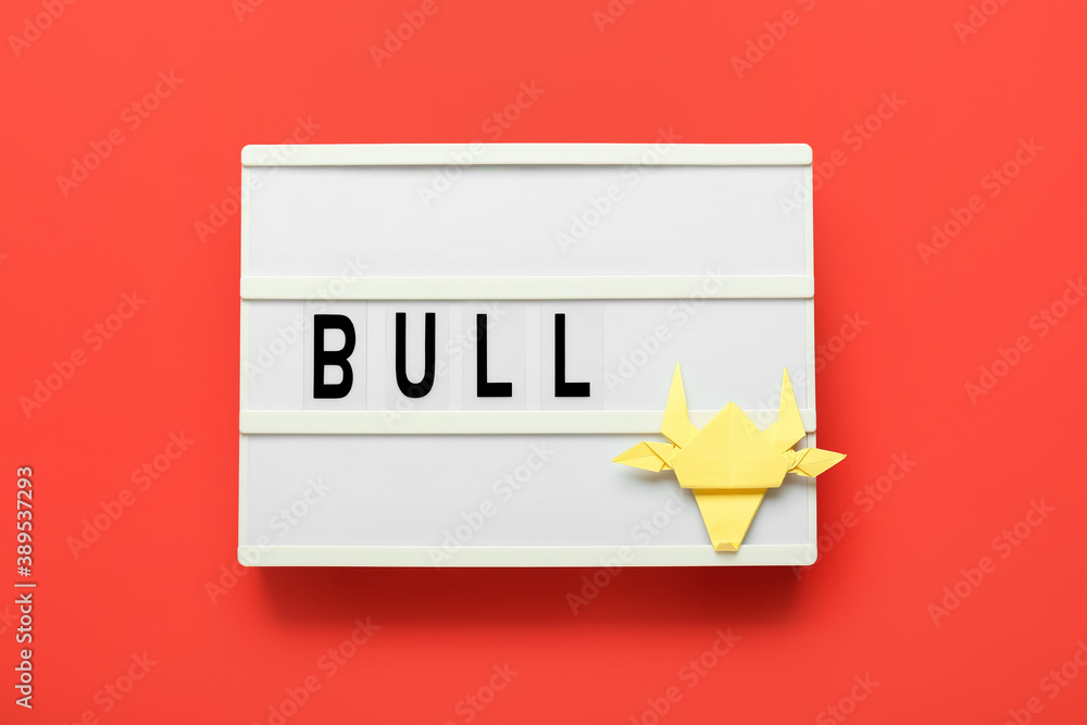 Board with origami bull as symbol of year 2021 on color background