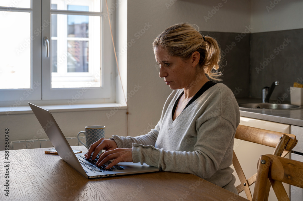 Femme dans sa cuisine en télétravail devant son ordinateur