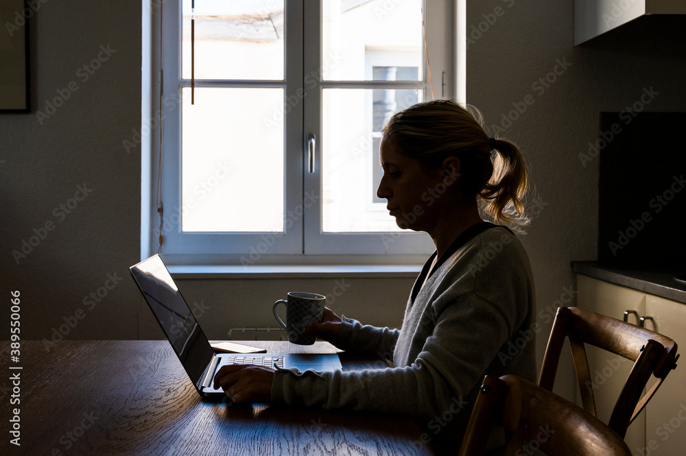 Femme dans sa cuisine en télétravail devant son ordinateur à contre-jour