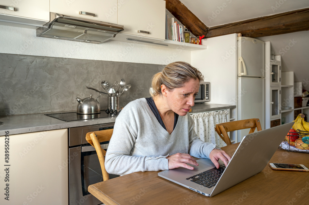 Femme dans sa cuisine en télétravail devant son ordinateur