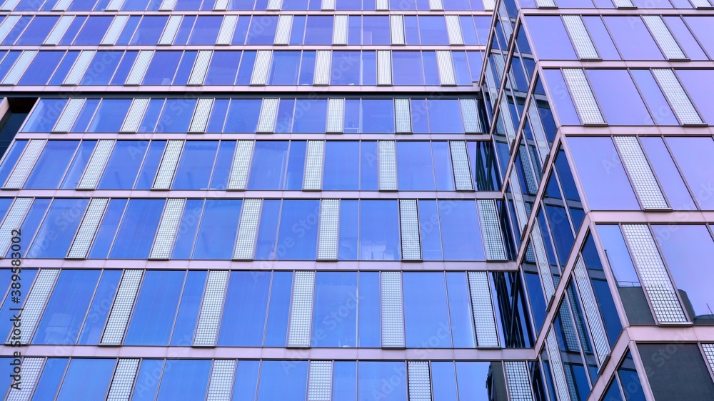 Blue curtain wall made of toned glass and steel constructions under blue sky. A fragment of a buildi