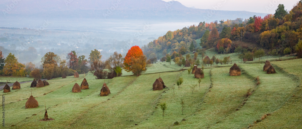 rural autumn landscape with fog and hay stacks