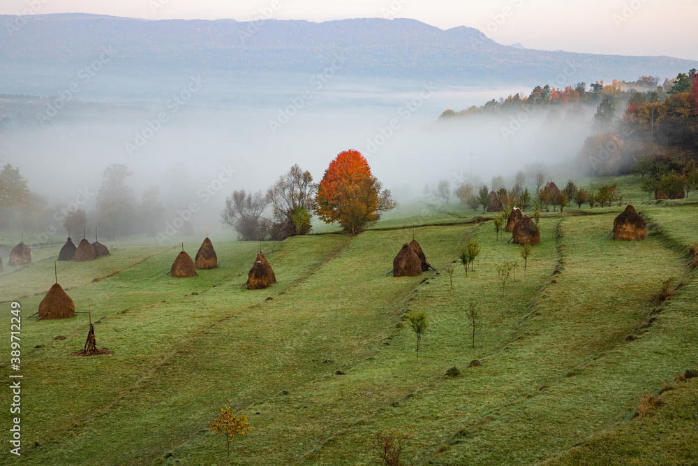 rural autumn landscape with fog and hay stacks