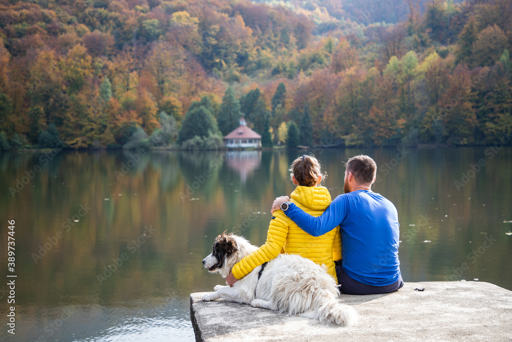 couple and dog sitting by beautiful autumn lake