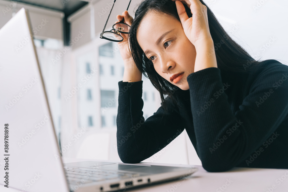 Image of stressed asian woman working from home on laptop looking worried, tired and overwhelmed