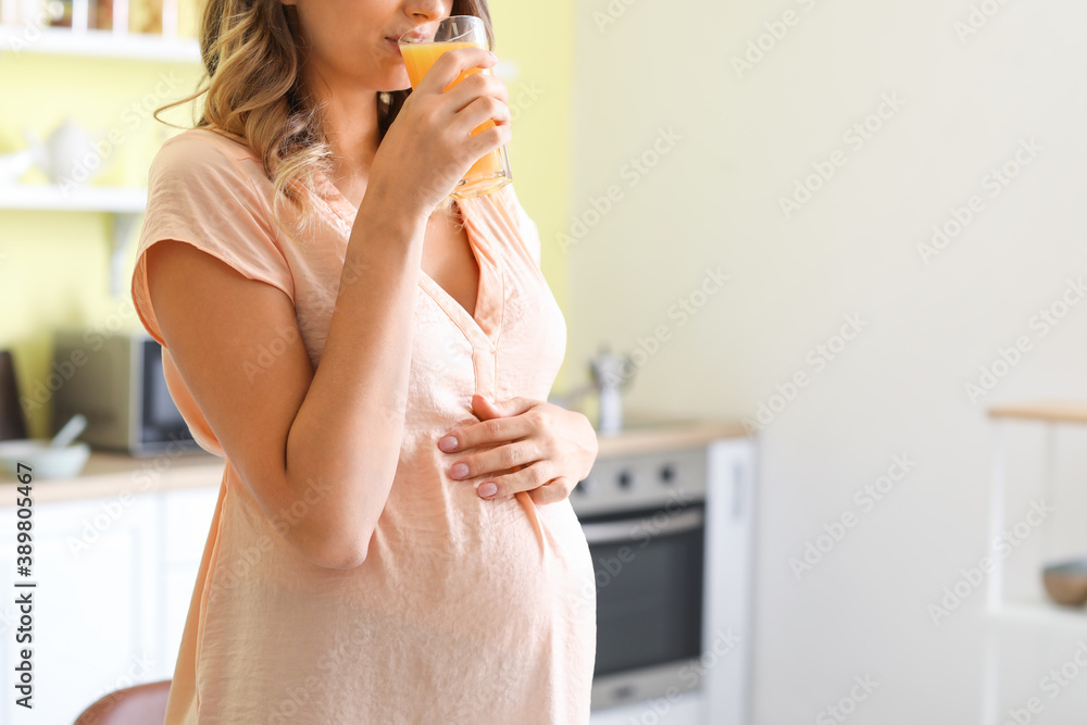 Beautiful pregnant woman drinking healthy juice in kitchen