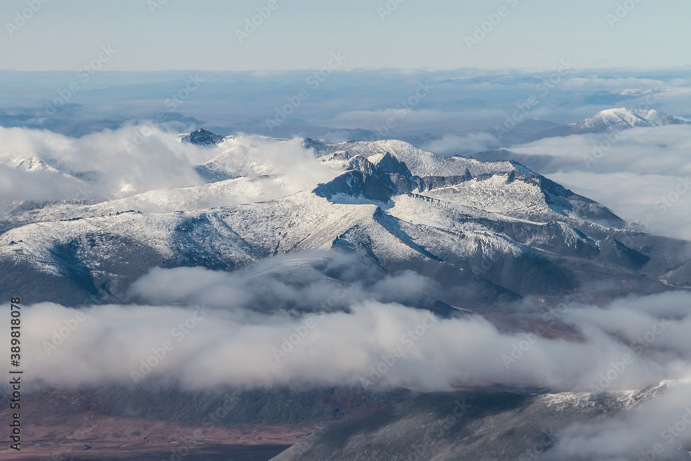 Aerial view of snow-capped mountain peaks. Top view of the mountain range among the clouds. Epic mou