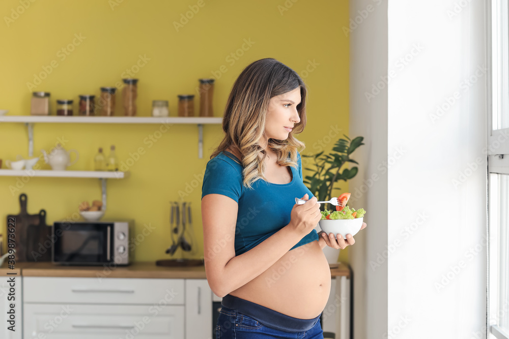 Beautiful pregnant woman eating healthy vegetable salad in kitchen