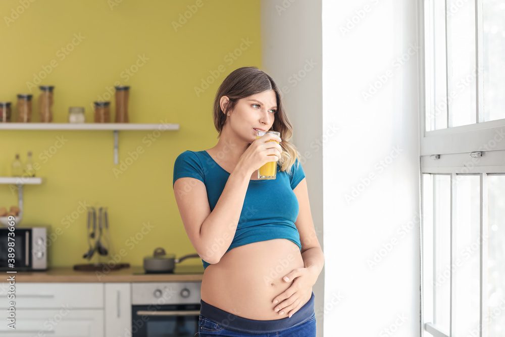 Beautiful pregnant woman drinking healthy juice in kitchen