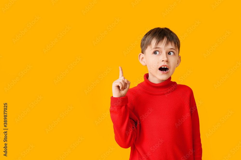 Cute little boy in autumn clothes pointing at something on color background