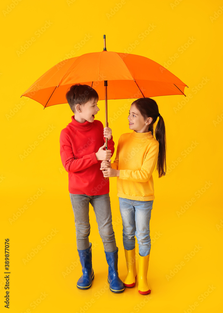 Cute little children in autumn clothes and with umbrella on color background